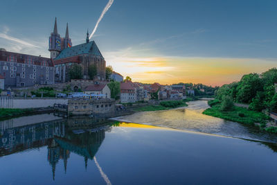 Buildings by river against sky during sunset