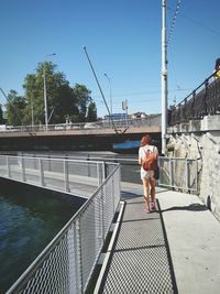 Rear view of woman standing on footbridge against clear sky