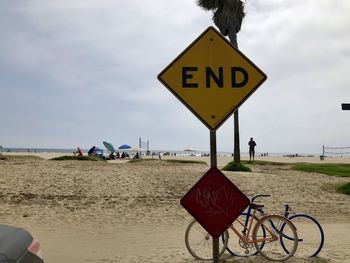 Information sign on road by beach against sky