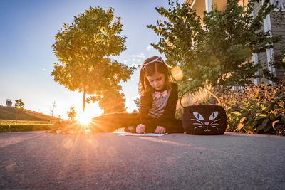 Young girl in a cat costume writes a note near a cat halloween bucket