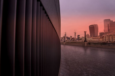 Bridge over river by buildings against sky during sunset