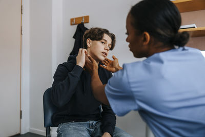 Female doctor checking neck of patient while sitting in medical examination room