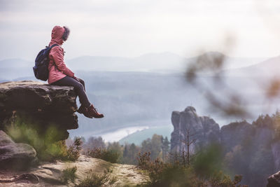 Full length of woman sitting on rock while looking at view