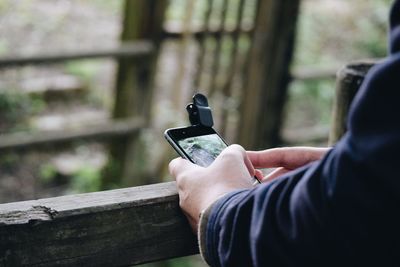 Cropped hands using phone on wooden railing