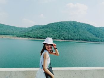 Young woman standing by lake against sky