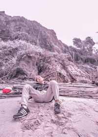 Young man sitting on land against mountain