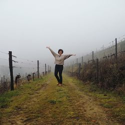 Woman with arms outstretched standing on footpath against sky