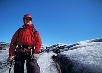 Man standing on snow covered landscape against clear blue sky