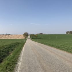 Empty road amidst field against sky