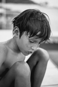 Young tanned boy, sitting by the sea, with water dripping from wet hair