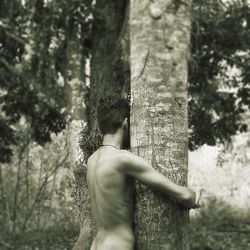 Naked man embracing tree trunk