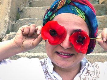 Close-up of woman covering eyes with red flowers