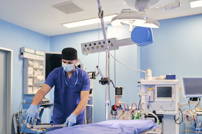 Male assistant wearing face mask adjusting operation table while standing in operation room at hospital