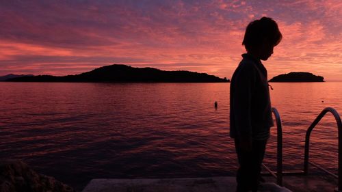 Silhouette man standing by sea against orange sky