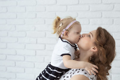Side view of mother kissing daughter against wall
