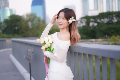 Portrait of young woman standing against railing