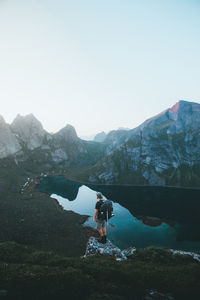 Man standing at lakeshore against mountains