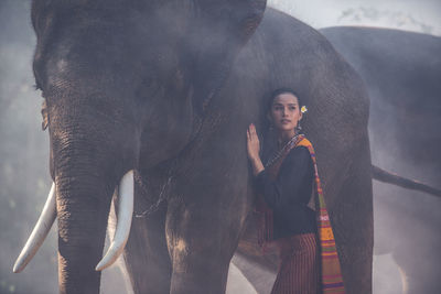 Young woman standing with elephant in forest