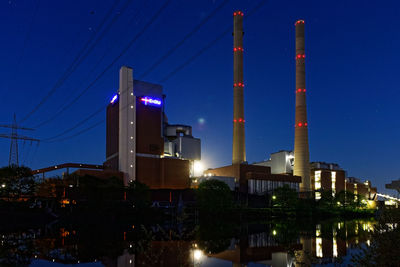 Illuminated factory against blue sky at night