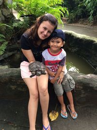 Portrait of mother with son holding tortoise while sitting on retaining wall
