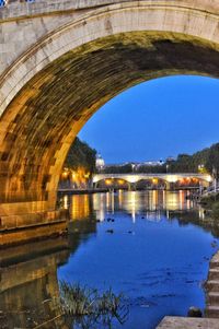 River by illuminated built structure against blue sky