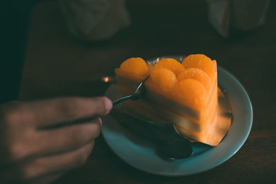 Cropped image of hand holding orange slice in plate
