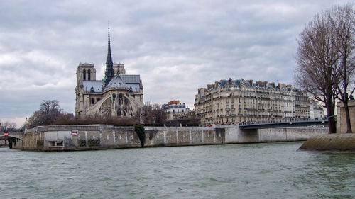 View of buildings by river against sky in city