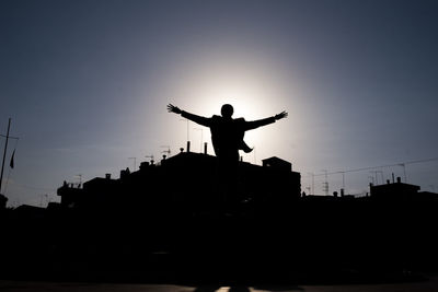 Silhouette of man with arms outstretched against buildings