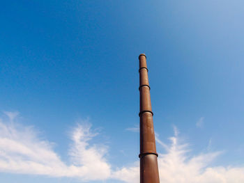 Tall industrial chimney taken from the ground on a sunny day with blue sky and beautiful clouds