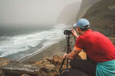 Man photographing sea with camera on rock at beach