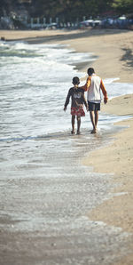 Rear view of mother and daughter walking on beach