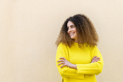 Happy woman standing with arms crossed in front of wall