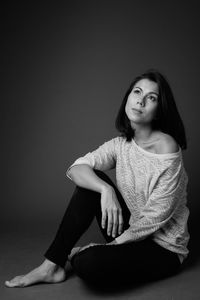 Portrait of young woman sitting against gray background