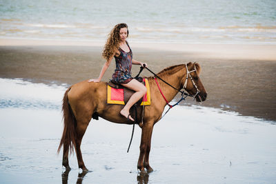 Full length of woman riding horse at beach