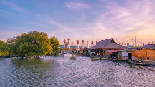 Scenic view of river by buildings against sky at sunset