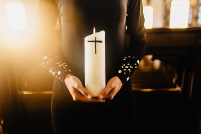 Midsection of woman holding illuminated candle at church