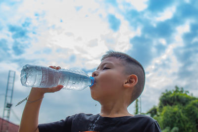 Boy drinking water from bottle against sky