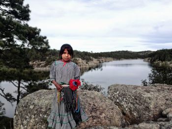 Portrait of smiling man standing on rock against lake