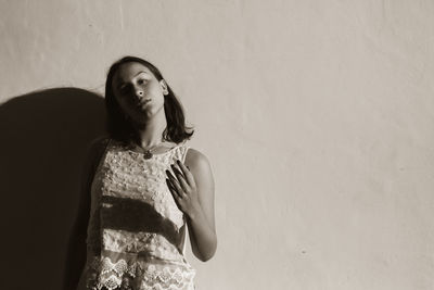 Young woman looking away while standing against wall