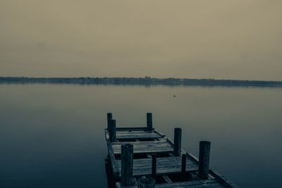 Wooden posts on jetty in lake against sky