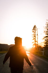 Rear view of silhouette man standing on road against sky during sunset