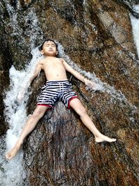 High angle view of boy lying on rock at beach