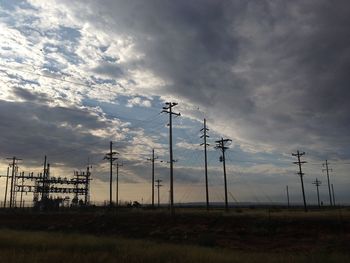 Electricity pylon on field against cloudy sky