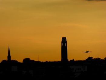 Silhouette tower by airplane flying in orange sky