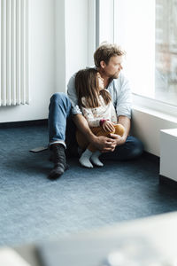 Father and daughter day dreaming by window at home