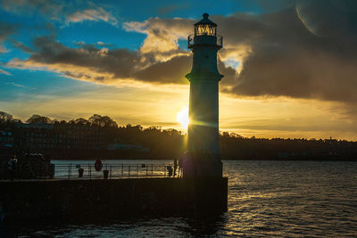 Lighthouse by sea against sky during sunset