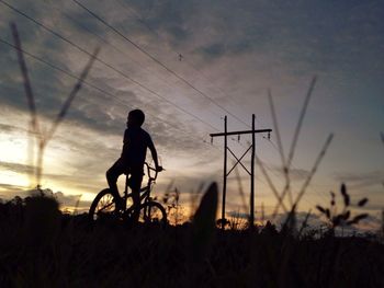 Silhouette man and bicycle on field against sky during sunset