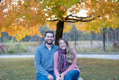 Portrait of smiling young woman sitting on tree during autumn