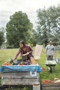 Mid adult woman arranging garden vegetables on table with man in background