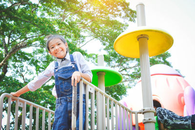 Low angle portrait of girl standing on play equipment at park